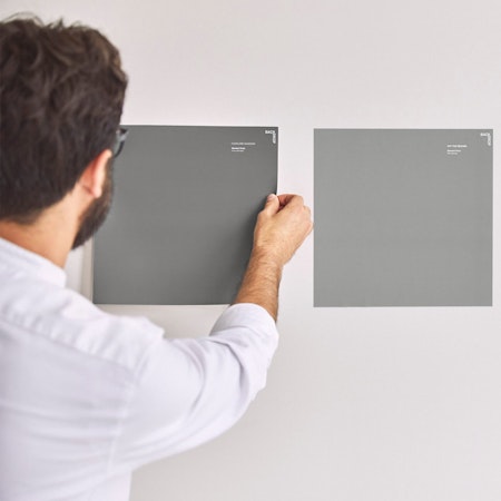 A person placing an adhesive sample swatch on a wall
