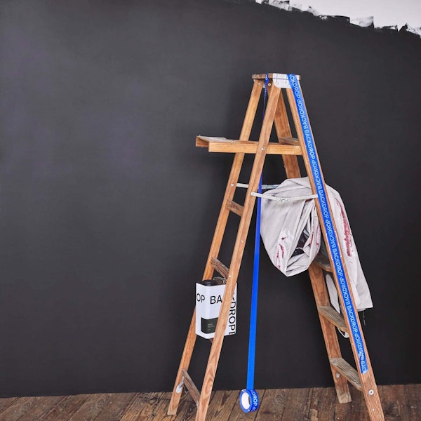 A ladder and paint supplies in front of a wall painted with DARK ARTS