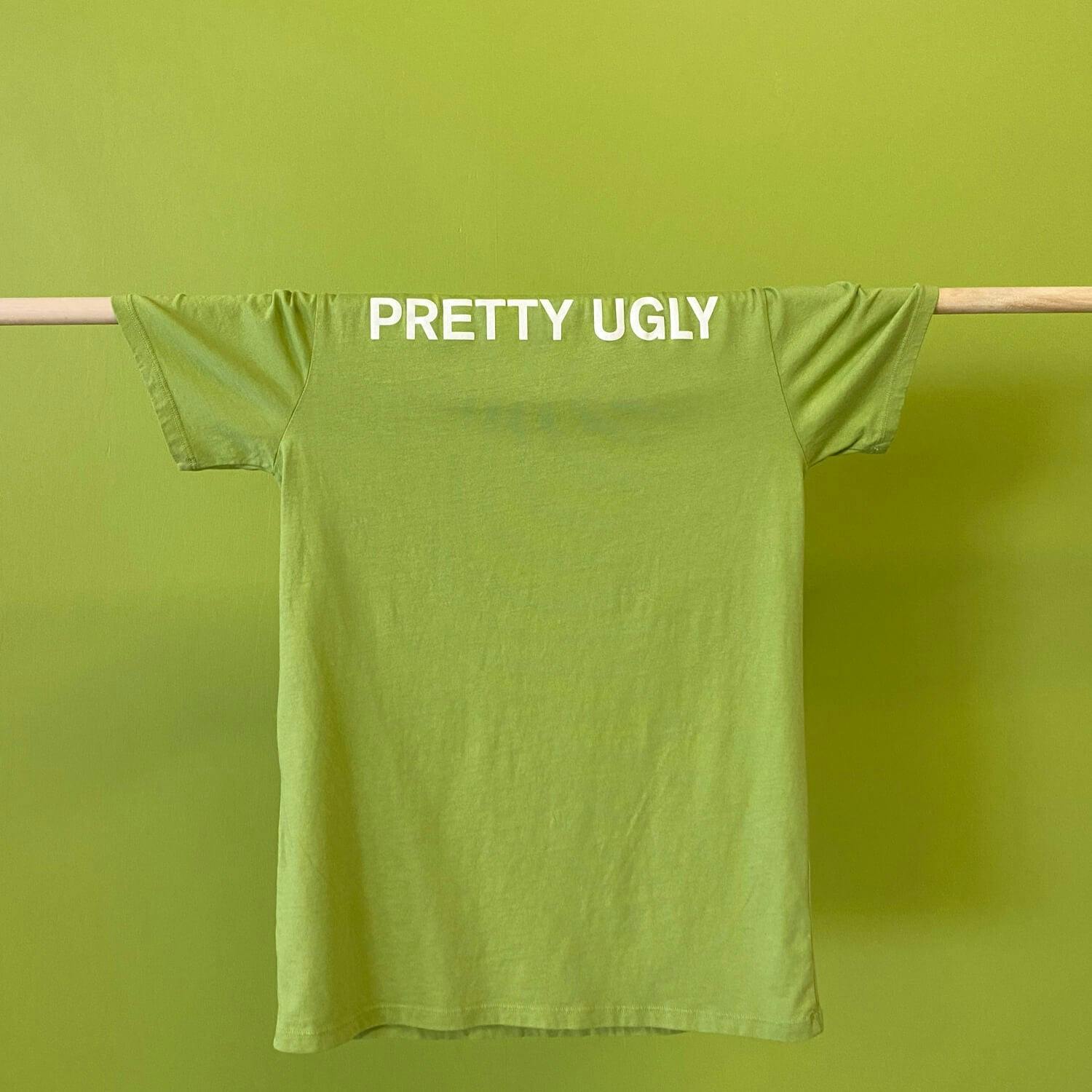 A t-shirt with the words "PRETTY UGLY" handing in front of a wall painted with PRETTY UGLY