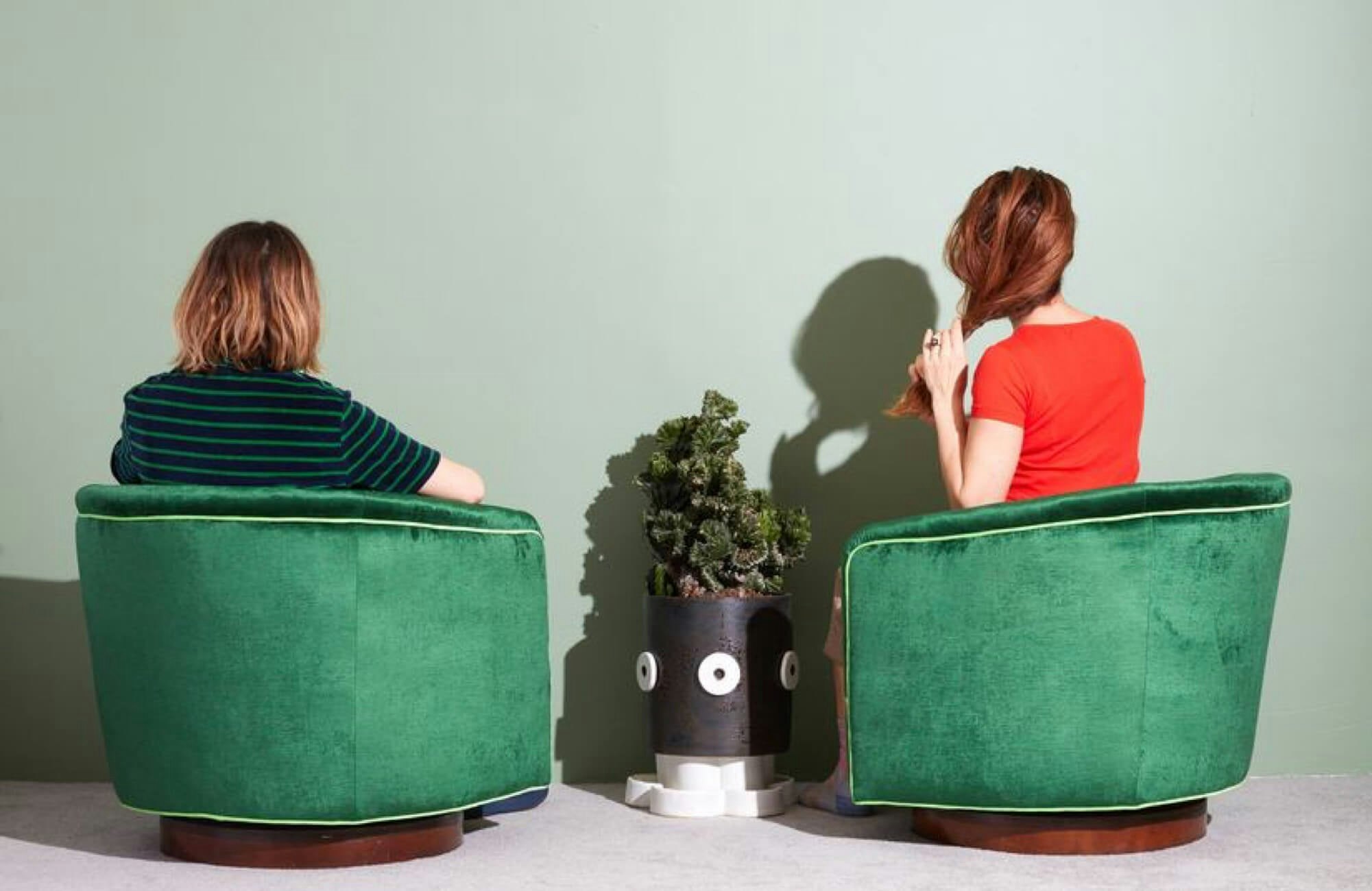 Two people sitting in green chairs facing away, towards a painted green wall