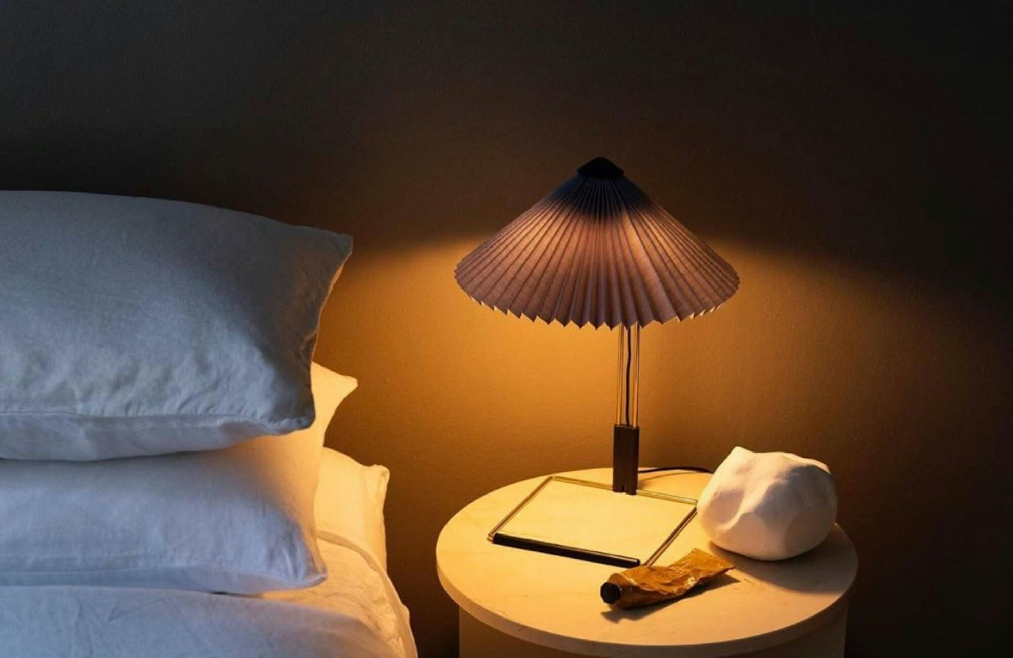 A lit lamp on a nightstand in a dark bedroom in front of a wall painted with SENTIMENTAL REASONS